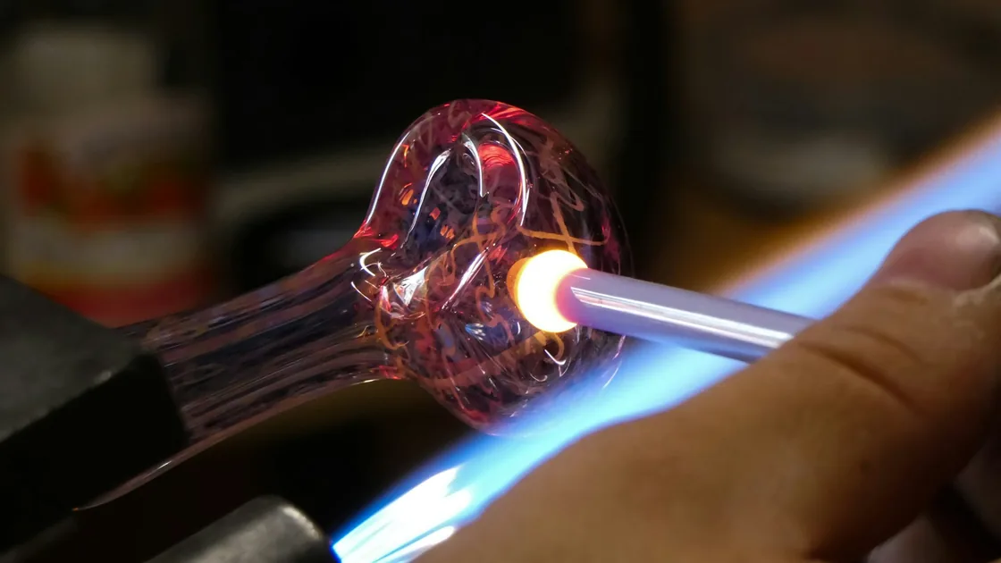 Varilla de vidrio caliente trabajada con la llama azul de un soplete de sobremesa en un banco de lampwork